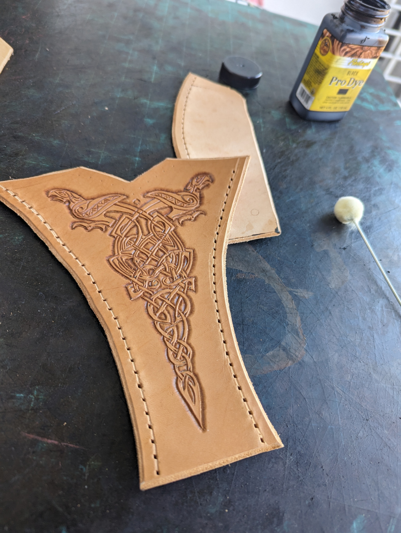 Natural leather bracer panel with a carved Mjolnir knotwork design beside dye supplies