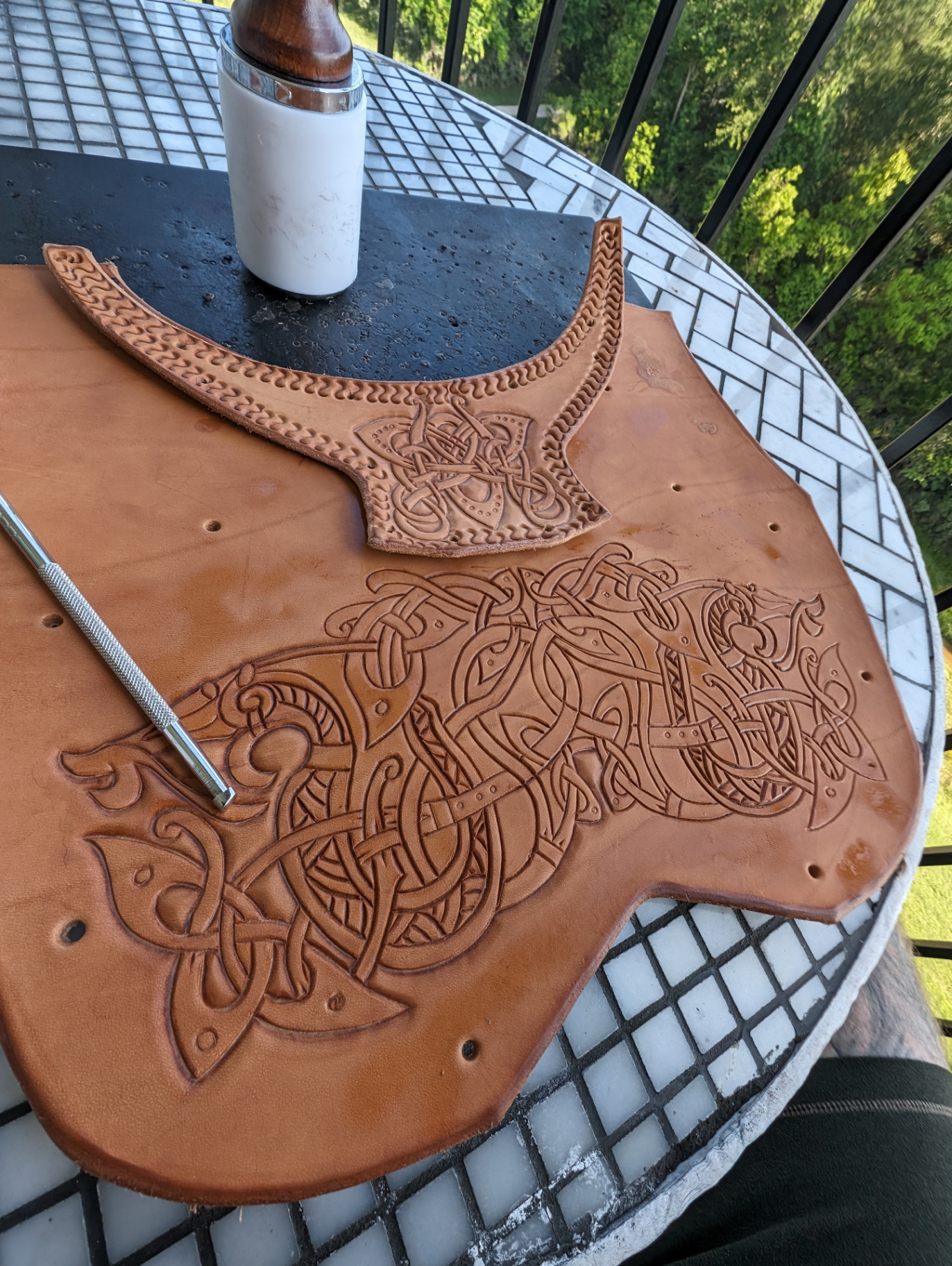 Large leather chest armor panel with carved knotwork beside a matching shoulder piece during the layout stage