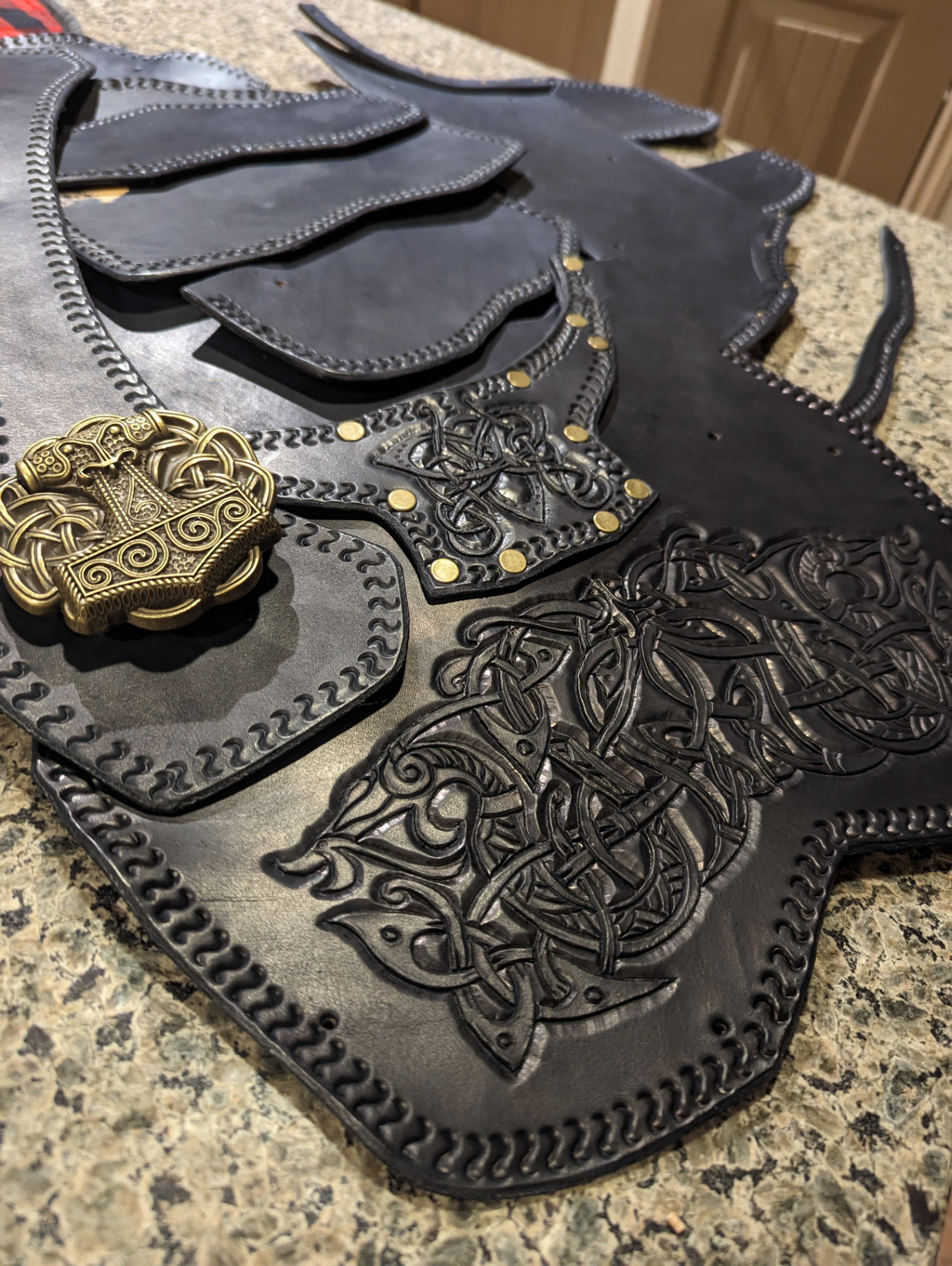 Finished black leather armor components with embossed knotwork and brass hardware laid out together
