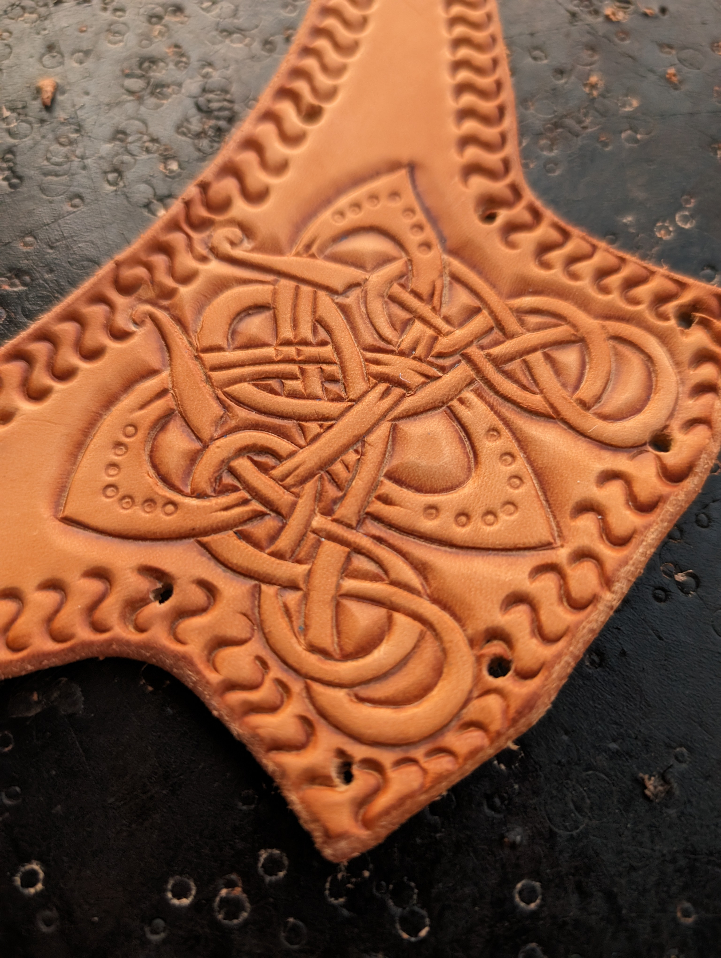 Close-up of intricate Celtic knotwork hand-tooled into a natural veg-tan leather axe-head shaped panel with braided border stamping