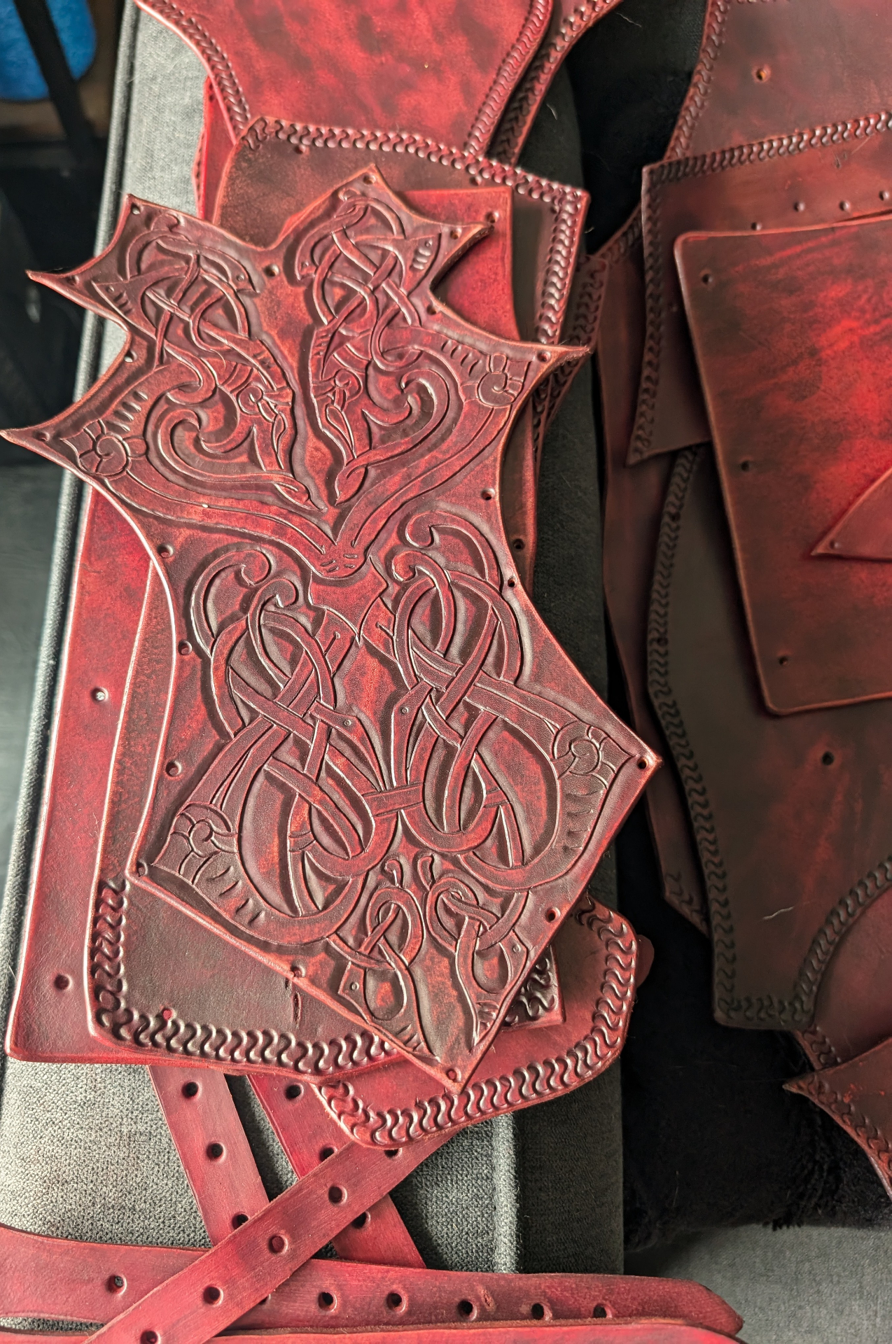 Red dyed leather armor panel with carved knotwork resting over matching leather components and straps